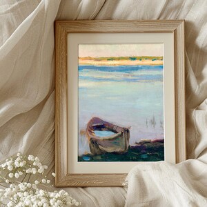 Framed painting of a boat on calm water, surrounded by soft beige fabric and delicate white flowers, evoking a serene and peaceful mood.