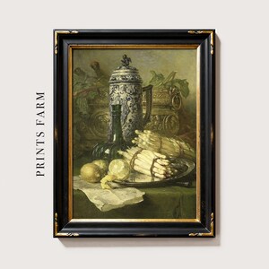 Framed painting of a still life featuring a decorative jug, wine bottle, lemons, and bundles of asparagus, all set on a green tablecloth.