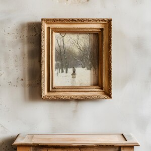 A vintage painting in an ornate gold frame hangs on a textured, weathered wall above a rustic wooden table. The painting depicts a snowy landscape with trees.