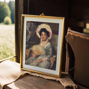 A framed portrait of a woman holding a fan, wearing a bonnet and a formal dress. It rests on a wooden surface, with a soft, natural backdrop.
