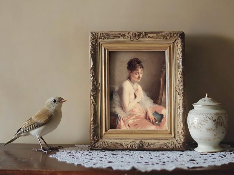 A delicate bird stands on a lace-covered table next to a vintage framed painting of a seated woman with a gentle expression, alongside an ornate ceramic jar.