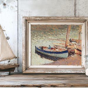 Framed impressionist painting of boats on a serene sea, displayed on a wooden shelf. Nearby, a model sailboat and a jar of sand create a coastal feel.