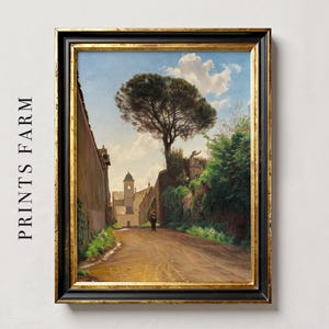 A framed oil painting depicting a narrow, cobblestone street lined with tall buildings and lush greenery. A lone figure walks down the street, with a large pine tree in the background.