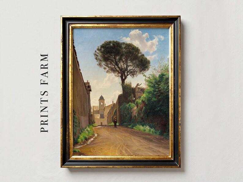 A framed oil painting depicting a narrow, cobblestone street lined with tall buildings and lush greenery. A lone figure walks down the street, with a large pine tree in the background.