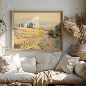 A cozy room with soft lighting features a landscape painting above a beige couch adorned with white pillows. Dried pampas grass adds a natural touch.