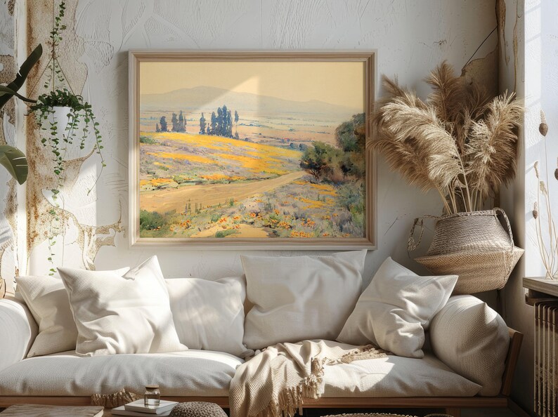 A cozy room with soft lighting features a landscape painting above a beige couch adorned with white pillows. Dried pampas grass adds a natural touch.