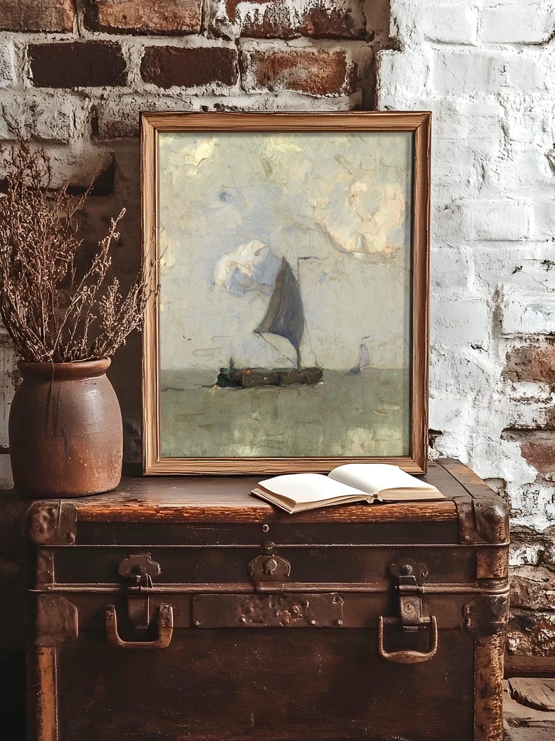 Framed artwork of a sailboat on calm waters rests on a vintage trunk. Nearby, a clay vase with dried branches and an open notebook create a rustic ambiance.