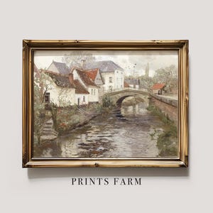 Framed painting of a serene village scene featuring rustic houses by a river, a stone bridge, and figures walking. The mood is tranquil and picturesque.