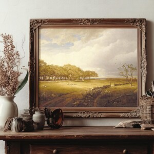 Framed landscape painting on a wooden shelf with vases, brushes, and dried flowers. It depicts a sunlit meadow with trees under a bright sky.