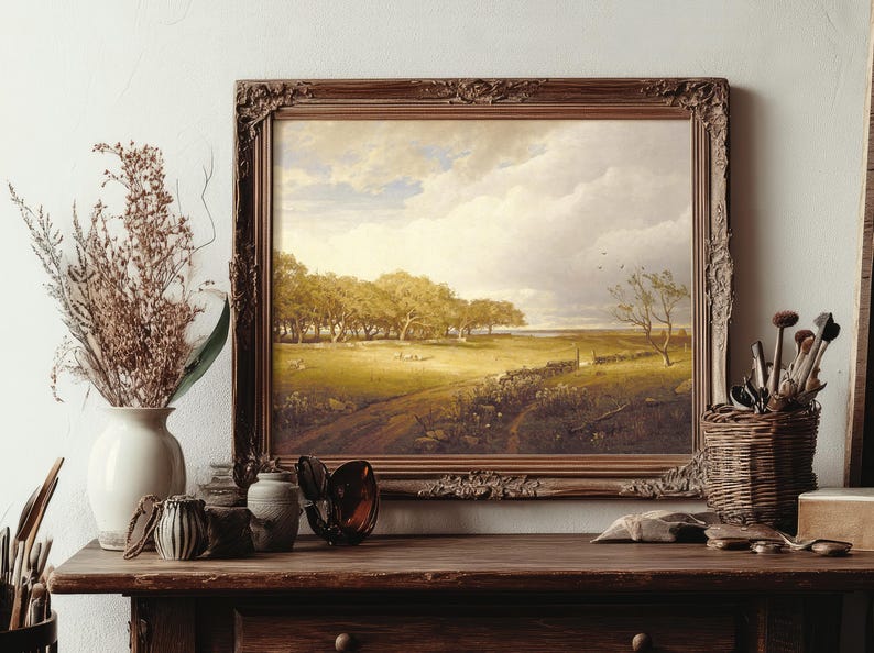 Framed landscape painting on a wooden shelf with vases, brushes, and dried flowers. It depicts a sunlit meadow with trees under a bright sky.
