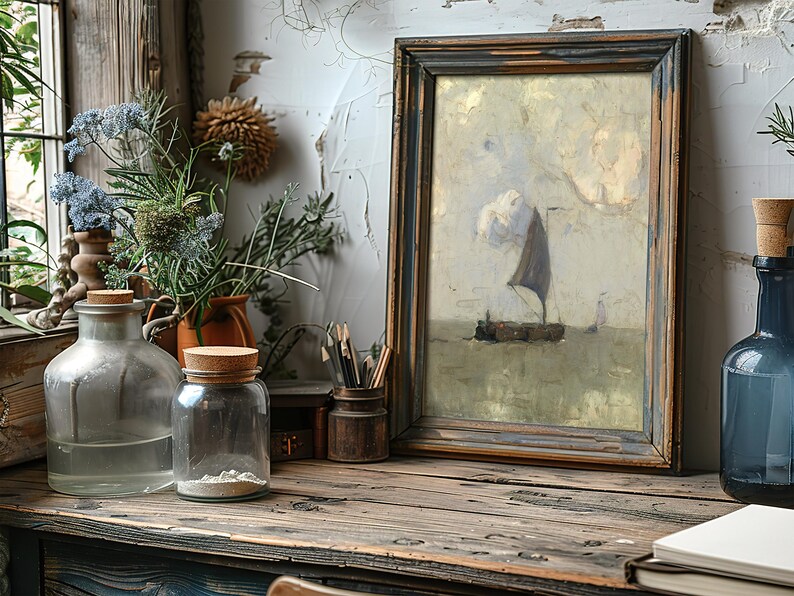 Rustic desk with framed painting of a sailboat, surrounded by glass jars, a notebook, and lush greenery in soft natural light. Cozy, creative atmosphere.
