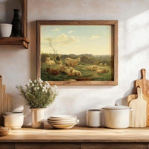 Framed painting of sheep in a serene landscape hangs on a kitchen wall. Below, a wooden counter holds white dishes, pots, and a vase with flowers.