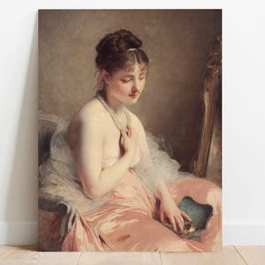 A graceful woman in a flowing pink dress gazes down contemplatively, holding a necklace. The setting is elegant, with warm tones and soft lighting.