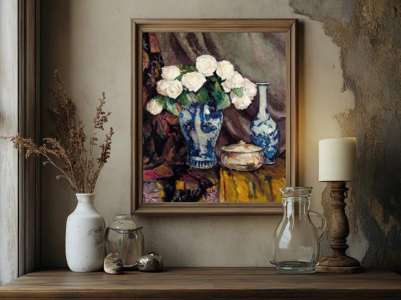 Framed painting of white roses in a blue vase on a textured wall. Surrounding objects include a lit candle, a clear glass bottle, and ceramic pots. Warm, cozy ambiance.