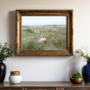 A landscape painting in an ornate gold frame hangs on a beige wall. Flanking it are vases with plants, including tulips and green foliage, on a wooden cabinet.