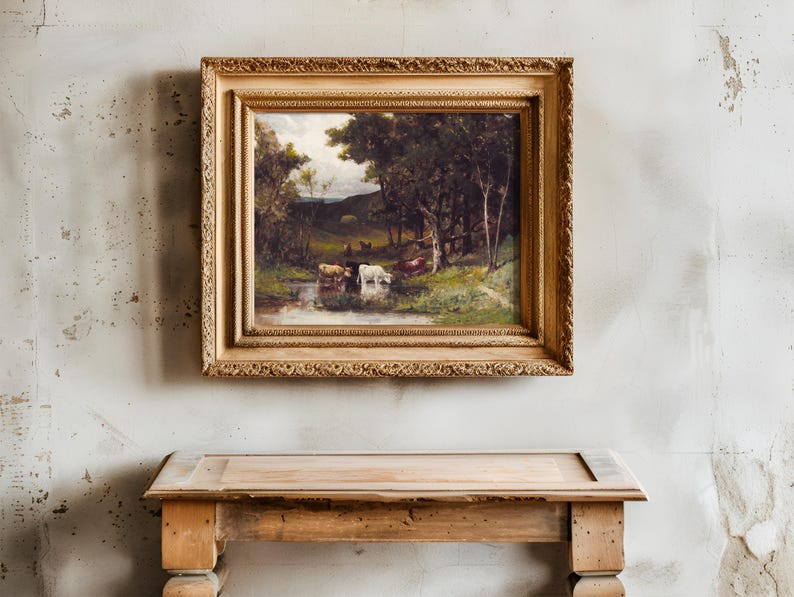 A rustic wooden table stands against a textured, aged wall with a framed pastoral painting above, depicting cattle by a stream under lush trees.