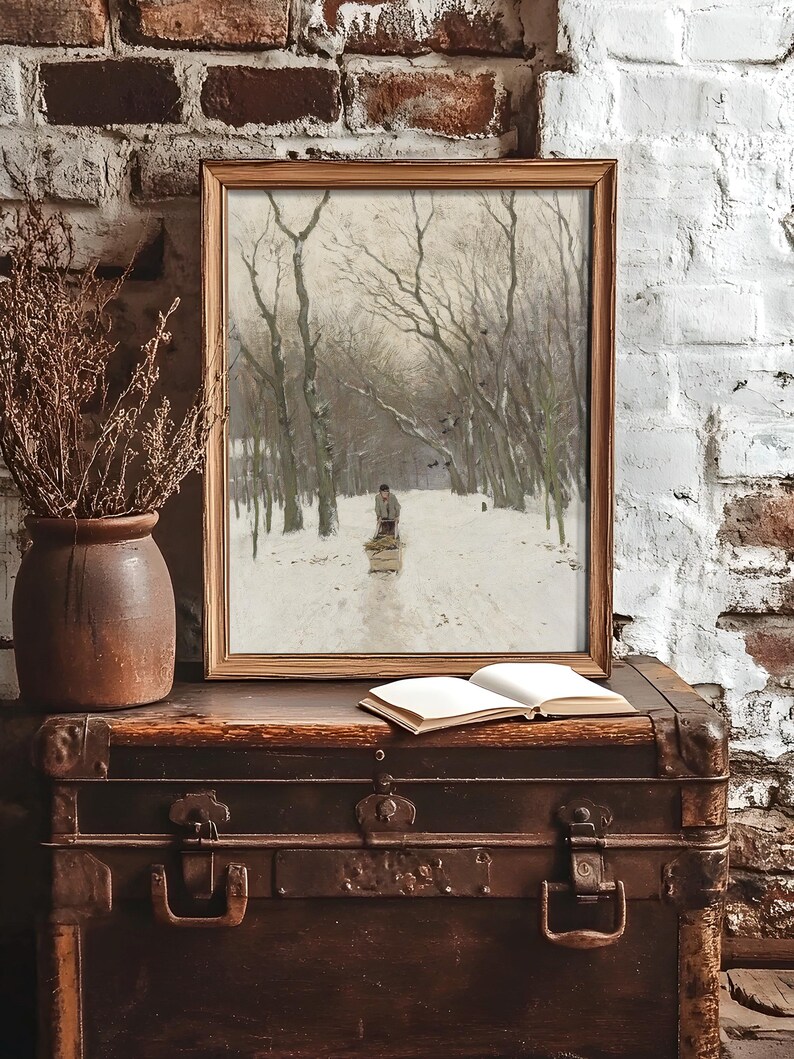 Framed winter scene on a rustic trunk against a brick wall. A painting depicts a snowy forest with a person on a path, creating a serene and nostalgic mood.