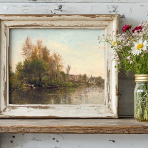 A rustic landscape painting in a distressed frame rests on a wooden shelf beside a mason jar of fresh wildflowers, creating a serene, vintage feel.