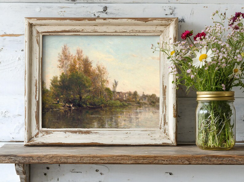 A rustic landscape painting in a distressed frame rests on a wooden shelf beside a mason jar of fresh wildflowers, creating a serene, vintage feel.
