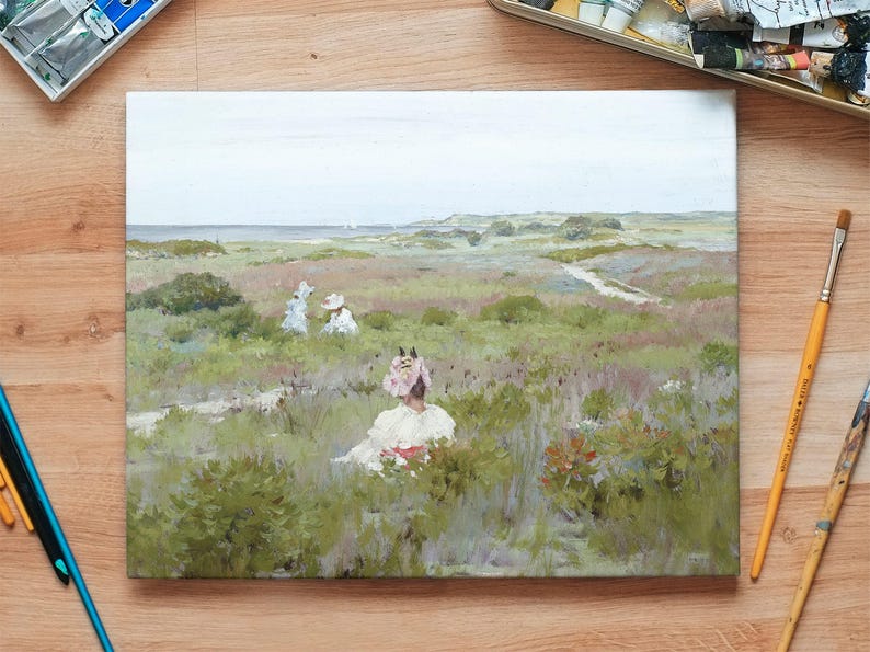 A landscape painting on a wooden table shows women in vintage dresses sitting in a lush, green field. Art supplies like paints and brushes surround the canvas.