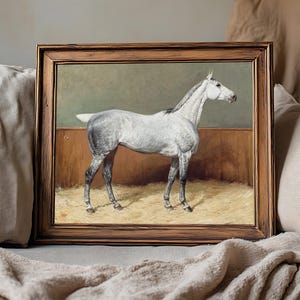 A framed painting of a white horse stands on a soft beige blanket. The horse is depicted in profile against a muted background, conveying calm and elegance.