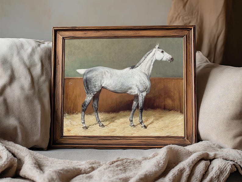 A framed painting of a white horse stands on a soft beige blanket. The horse is depicted in profile against a muted background, conveying calm and elegance.