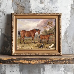 A framed painting of two horses and two dogs in a pastoral setting rests on a rustic wooden shelf against a textured, distressed wall.