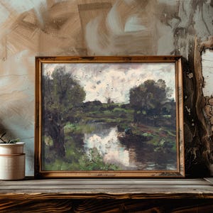 A framed landscape painting of a river and trees rests on a rustic wood shelf beside a potted plant. The backdrop is a textured, earthy wall.