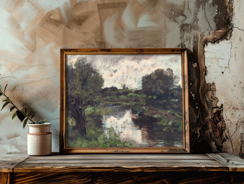 A framed landscape painting of a river and trees rests on a rustic wood shelf beside a potted plant. The backdrop is a textured, earthy wall.