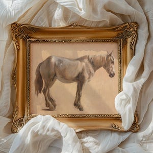 A framed painting of a horse with a dark mane set against a beige background. The ornate gold frame lies atop soft, flowing white fabric, creating an elegant and serene atmosphere.