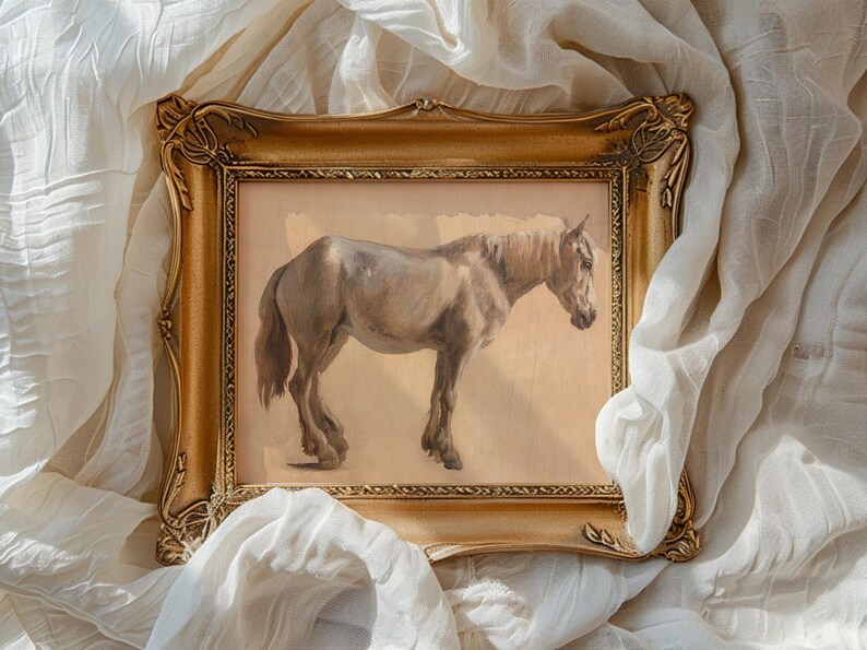 A framed painting of a horse with a dark mane set against a beige background. The ornate gold frame lies atop soft, flowing white fabric, creating an elegant and serene atmosphere.
