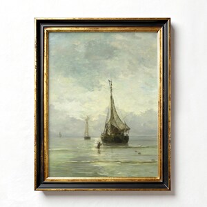 A framed oil painting depicting a seascape with two sailboats on a calm, blue-grey sea. The sky is a light blue with white clouds. The painting is in a dark wood frame with a gold trim.