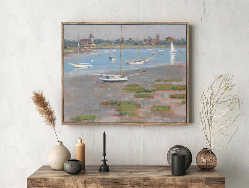 A painting of sailboats on a calm lake, with green patches and a distant town under a cloudy sky, hangs above a wooden table with vases and candles.