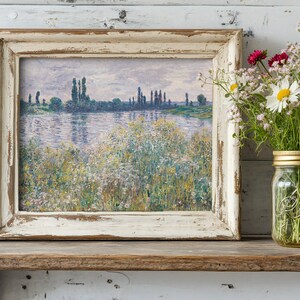 A rustic shelf displays a framed painting of a serene river landscape with tall trees, alongside a glass jar of colorful wildflowers, conveying tranquility.