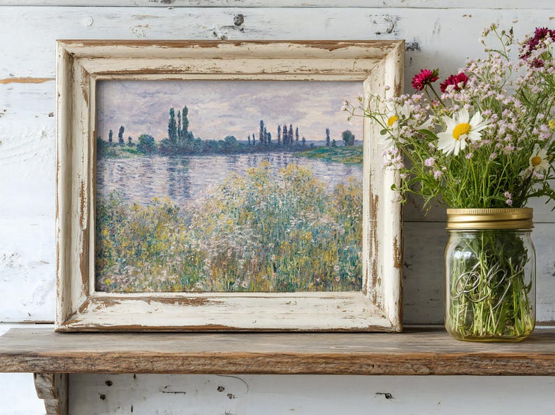 A rustic shelf displays a framed painting of a serene river landscape with tall trees, alongside a glass jar of colorful wildflowers, conveying tranquility.