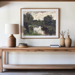 A minimalist room with a wooden console table. It holds a ceramic lamp and vases. Above, a framed landscape painting adds a serene touch.