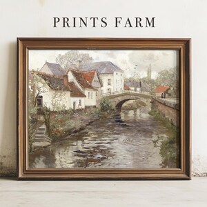 Framed painting of a serene village scene with a river, arched stone bridge, and cottages with red roofs, conveying a peaceful, rustic vibe.