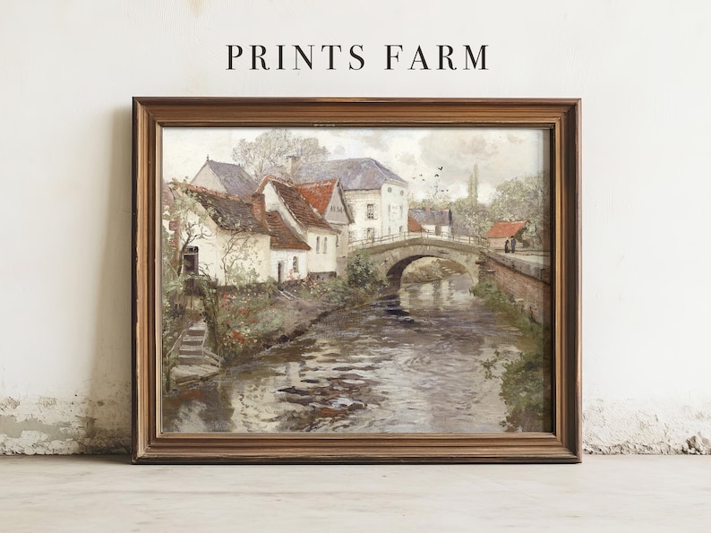 Framed painting of a serene village scene with a river, arched stone bridge, and cottages with red roofs, conveying a peaceful, rustic vibe.