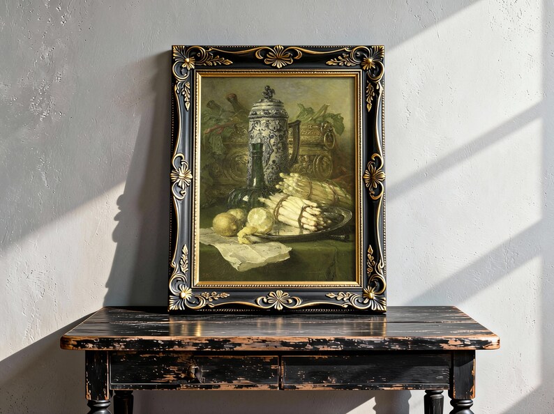 A framed still life painting on a rustic wooden table shows a decorative jug, a wine bottle, and a platter with asparagus and lemons. Soft sunlight casts shadows on a textured wall.