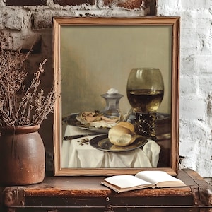 Framed still life painting on rustic shelf with bread, a glass of wine, and a dish. Nearby, a vase holds dried branches. An open book lies on the shelf, creating a vintage, serene atmosphere.