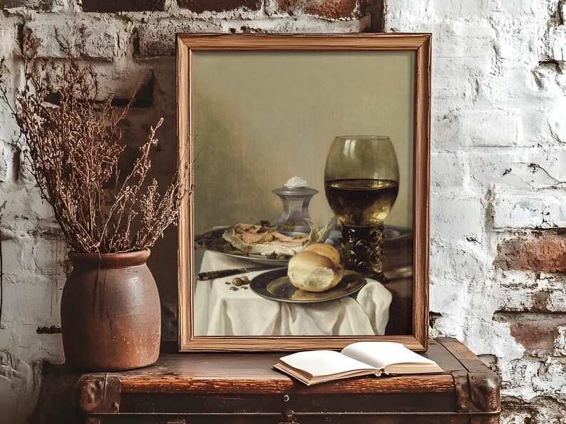 Framed still life painting on rustic shelf with bread, a glass of wine, and a dish. Nearby, a vase holds dried branches. An open book lies on the shelf, creating a vintage, serene atmosphere.