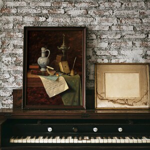 A vintage-style, dark wood, upright piano with a white and black keyboard. The piano is decorated with two framed pictures, one with a still life of a pitcher, a lamp, and a scroll, and the other with a blank white space.