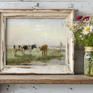 A rustic painting of two cows in a field is framed in worn wood, sitting on a shelf beside a mason jar filled with wildflowers, evoking calm and nostalgia.