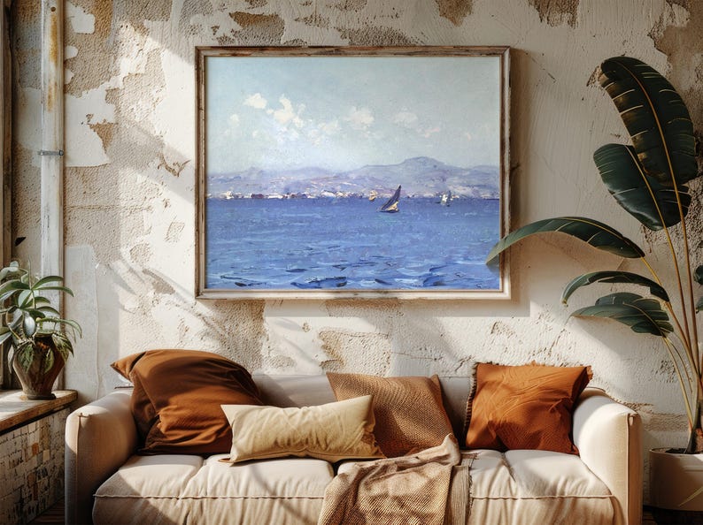 Cozy living room with a beige sofa, rust-colored cushions, and a blanket. A sea landscape painting hangs on a textured wall, evoking tranquility.