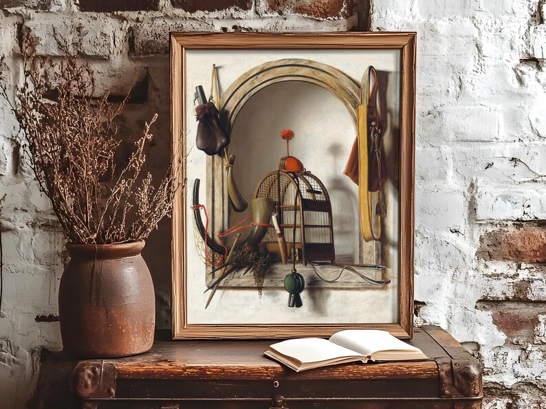 A rustic setting features a framed painting of a still life with a pomegranate, dried fruits, and a birdcage on a stone ledge. Beside it, dried branches in a clay vase and an open book rest on a wooden chest against a textured white brick wall, evoking a vintage and cozy ambiance.