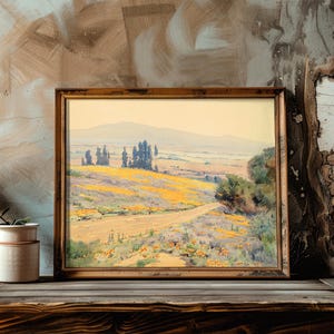 Framed landscape painting on a rustic wooden shelf with cracked textured wall; soft hues of yellows and greens evoke a serene, pastoral scene.