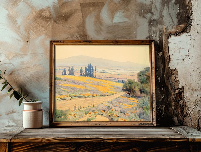 Framed landscape painting on a rustic wooden shelf with cracked textured wall; soft hues of yellows and greens evoke a serene, pastoral scene.