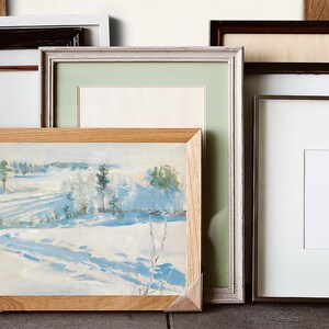 Various picture frames are arranged together, with one frame displaying a serene snowy landscape painting. The tones are soft, evoking a calm winter feel.