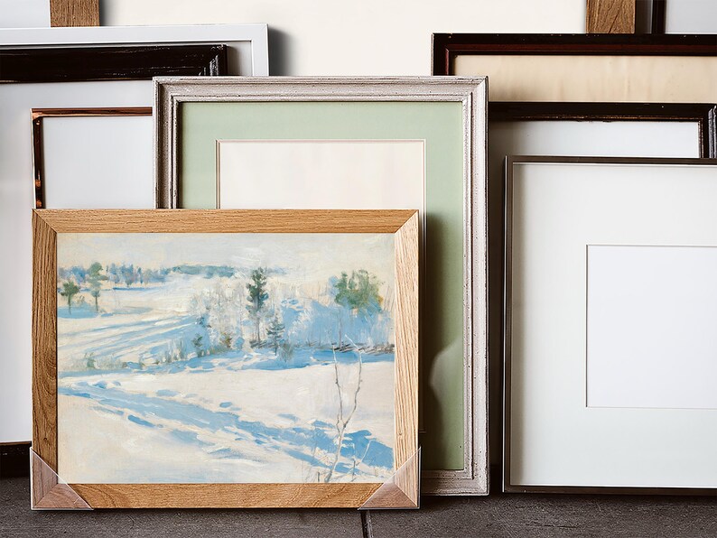 Various picture frames are arranged together, with one frame displaying a serene snowy landscape painting. The tones are soft, evoking a calm winter feel.