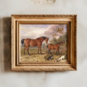 A framed painting features two horses standing on grassy land with two dogs lying nearby. The sky is cloudy, and a tree is in the background.